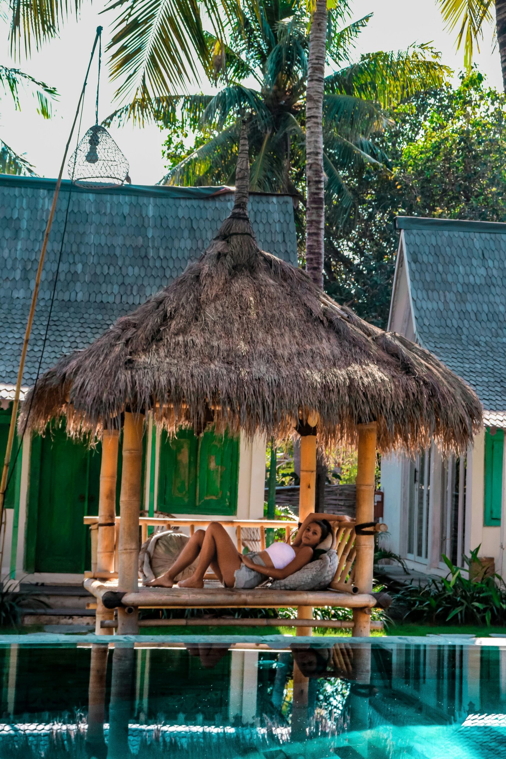 A woman relaxing in a tropical Bali resort hut by the pool surrounded by palm trees.