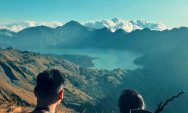 Two hikers enjoy a breathtaking view of Mount Rinjani's crater lake in Indonesia's Nusa Tenggara Barat.